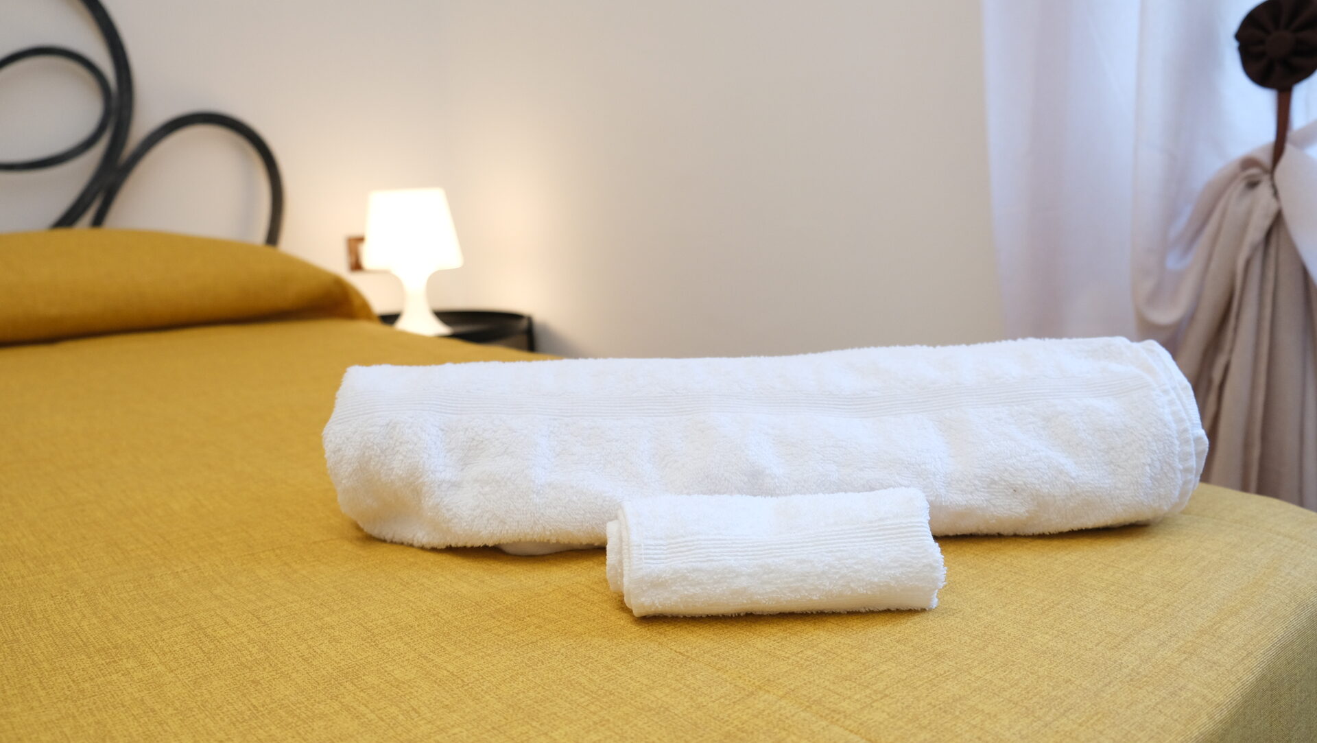 Letto con testiera in ferro battuto e biancheria color senape