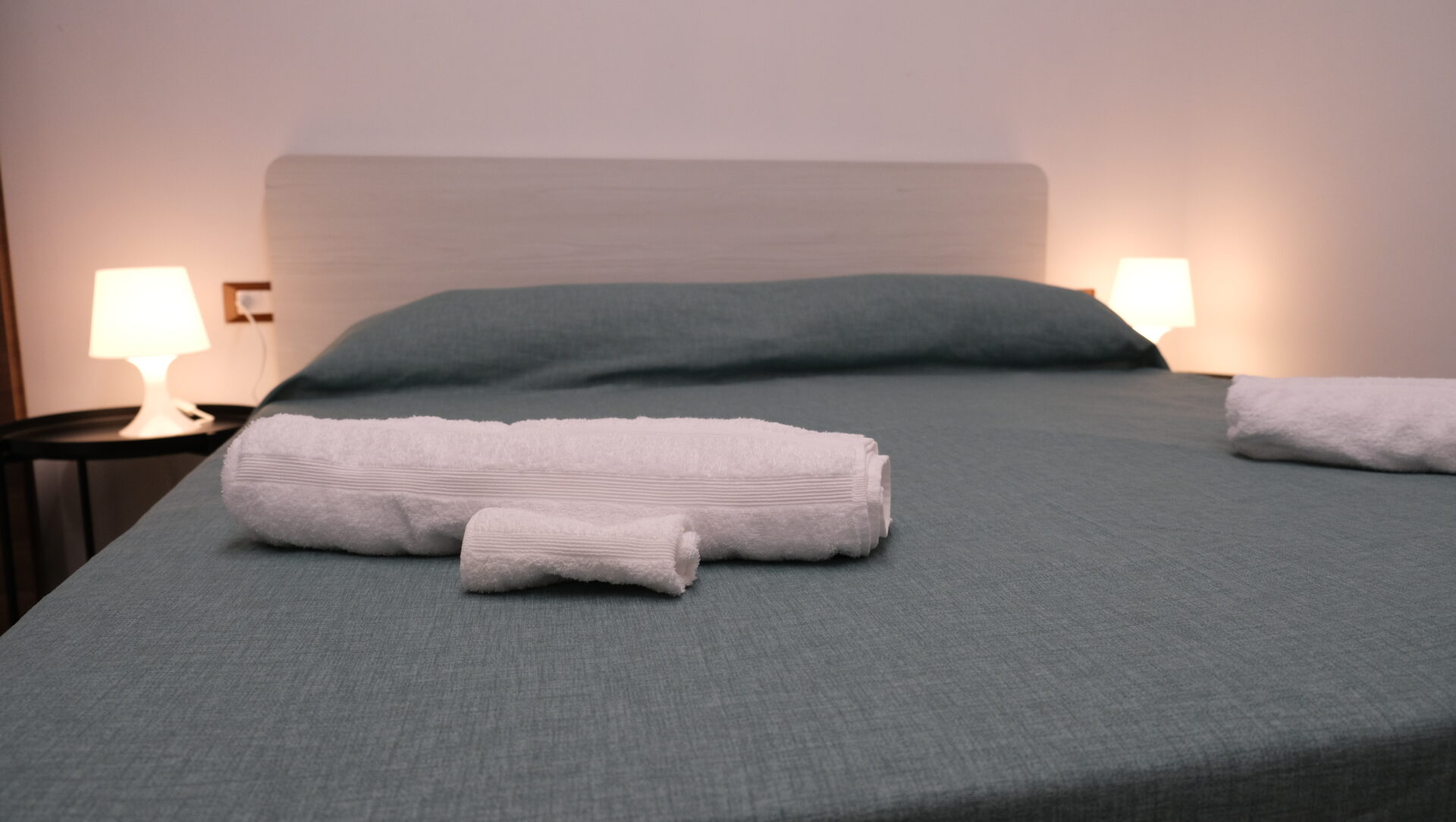 Letto con biancheria verde petrolio e asciugamani preparati